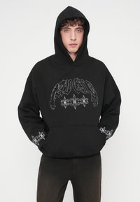 Μαύρο φαρδύ φούτερ φτιαγμένο από μίγμα βαμβακιού. Διαθέτει μεγάλο ασημένιο γραφικό στο μπροστινό μέρος και ασημένια λουλουδάτα σχέδια στα μανίκια.