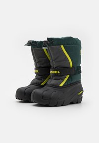 Botas de invierno aisladas en verde y gris con suela de goma, parte superior ajustable y detalles en amarillo brillante. Presentan un diseño acolchado y texturizado.