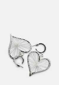 Orecchini ad anello a forma di cuore in tonalità argento con un intricato design di filo simile a un filo e chiusura a perno su uno sfondo bianco.