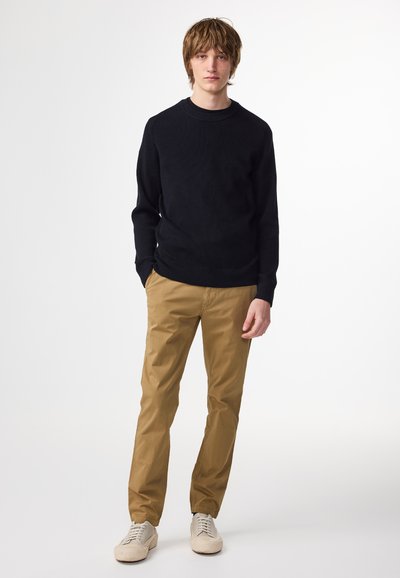 Svart ribbad tröja, beige chinos och ljusa sneakers. Enkel design med rund halsringning och texturerat stickat tyg.