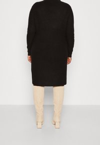 Černé pletené dlouhé šaty s dlouhými rukávy a kulatým výstřihem, doplněné béžovými kozačkami nad kolena s masivním podpatkem.