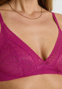 Brassière en dentelle fuchsia avec une forme triangulaire, des bords festonnés et un motif floral délicat ; bretelles roses réglables.