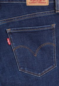 Mörkblå denimjeans med ett klassiskt bakficka som har en signatur röd Levi's-flik och kontrasterande gul sömnad.