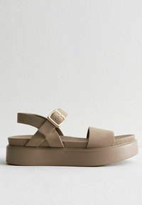 Sandalo platform beige con cinturini incrociati in tessuto e una cinghia posteriore con fibbia. Presenta una parte superiore in morbido camoscio sintetico e una suola piatta solida.
