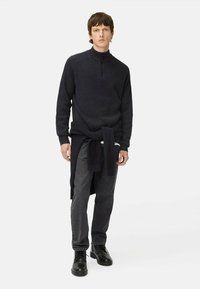 Dunkelblaue, gestrickte Zip-up-Pullover mit geripptem Muster, kombiniert mit grauen Jeans und schwarzen Schnürstiefeln, zusätzlich mit einem weiteren Pullover, der um die Taille gebunden ist.
