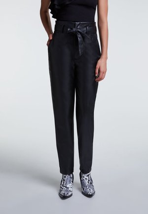 Schwarze Lederhose mit tailliertem Bund, mit glatter Textur und geradem Schnitt. Kombiniert mit gemusterten Knöchelstiefeln.