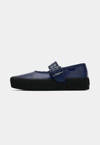 Marineblauwe Mary Jane-schoen met een dikke zwarte geribbelde zool en een verstelbare riem met gesp, gekenmerkt met het Vans-logo aan de zijkant.