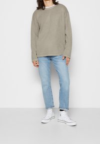 Tight, ribbad olivgrön långärmad skjorta i kombination med ljusblå raka jeans och vita högklackade sneakers.