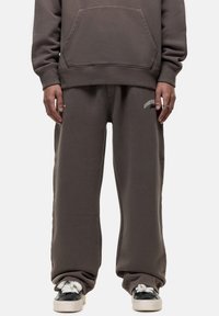 Dunkelgrauer Hoodie mit Kängurutasche, kombiniert mit lockeren Sweatpants in passendem Design, die ein weißes Logo auf dem linken Oberschenkel tragen.