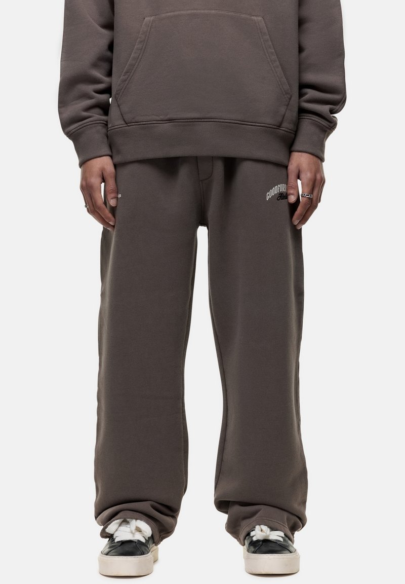 Dunkelgrauer Hoodie mit Kängurutasche, kombiniert mit lockeren Sweatpants in passendem Design, die ein weißes Logo auf dem linken Oberschenkel tragen.