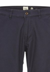 Pantalons en coton bleu marine avec une fermeture à bouton, une braguette zippée et des poches avant. Détails de couture visibles et étiquette en tissu sur la taille.