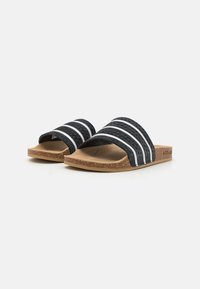 Svart sandaler med tre hvite striper, teksturert syntetisk overdel, korksåle og flat såle. Enkelt, åpent tådesign.
