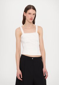 Haut blanc court avec encolure carrée, accents en dentelle et motifs texturés. Assorti à un pantalon noir taille haute. Design simple.