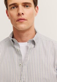 Camicia a righe in tessuto leggero, con righe verticali blu e crema, colletto a punta e bottoni visibili al collo.