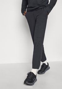 Vīriešu tumši pelēki bikses ar šauru dizainu, kas ietver plakanu priekšpusi, sānu kabatas un ar rāvējspagatu slēgtu kravu kabatu uz augšstilba. Valkātas ar melniem sporta apaviem.