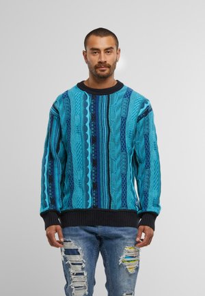 Mehrfarbiger gestrickter Pullover mit türkisfarbenen, blauen und schwarzen Mustern, versehen mit strukturierten Zopf-Details sowie gerippten Bündchen und Saum.
