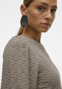 Elemento grigio testurizzato con una silhouette adattata. Grandi orecchini astratti neri. Pella liscia e tono della pelle uniforme con i capelli lisci in uno stile semplice.