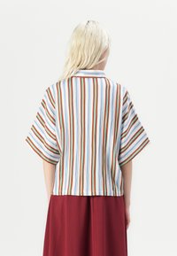 Camicia a maniche corte a righe con colletto; presenta righe blu, rosse e verdi su sfondo bianco; vestibilità ampia, tessuto leggero.