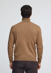 Brun polotröja i mjukt tyg, med figursydd design, ribbade muddar och slät yta, sedd bakifrån.