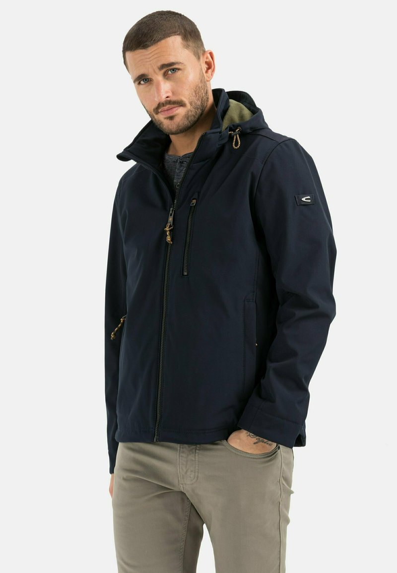 Veste à capuche bleu marine avec fermeture éclair à l'avant, cordon de serrage ajustable et deux poches zippées. Matière lisse et résistante à l'eau, design ajusté.