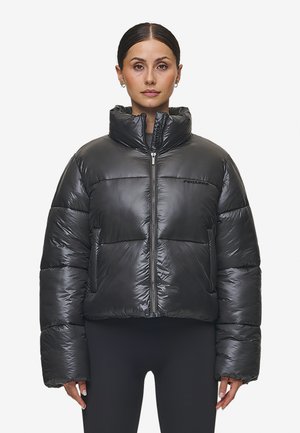 Zwarte pufferjack met hoge kraag, ritssluiting aan de voorkant, doorgestikte design en zachte, glanzende buitenkant; inclusief zichtbaar logo op de borst.