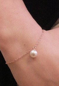 Bracciale a catena in oro rosa con una singola goccia di perla bianca, design aderente con una superficie liscia e lucida.