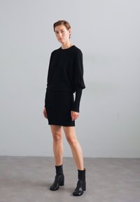 Completo in maglia nera composto da maglione e gonna, con maniche lunghe, silhouette aderente e texture liscia. Completo abbinato a stivaletti alla caviglia.