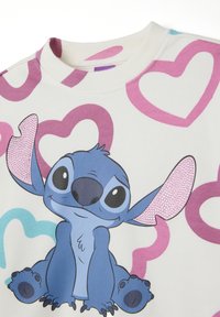 Sudadera de color crema claro con un personaje de dibujos animados de pelaje azul y acentos en rosa, rodeado de grandes corazones en rosa y turquesa.