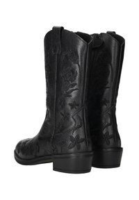 Een paar zwarte leren laarzen tot halverwege de kuit met lage hakken en gegraveerde bloempatronen op een witte achtergrond.