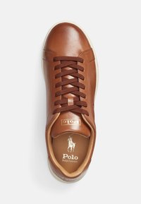 Bruna lädersneakers med rund tå, bruna snören och en vit gummisula. Funktioner med präglad logotyp på tungan och insidan. Slät textur.