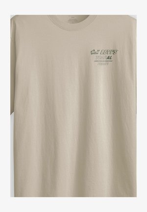 Camiseta beige de corte holgado con texto verde en el pecho que dice "¡Llama hoy a LEVI'S TOADAL para jardinería y reparaciones del hogar!"