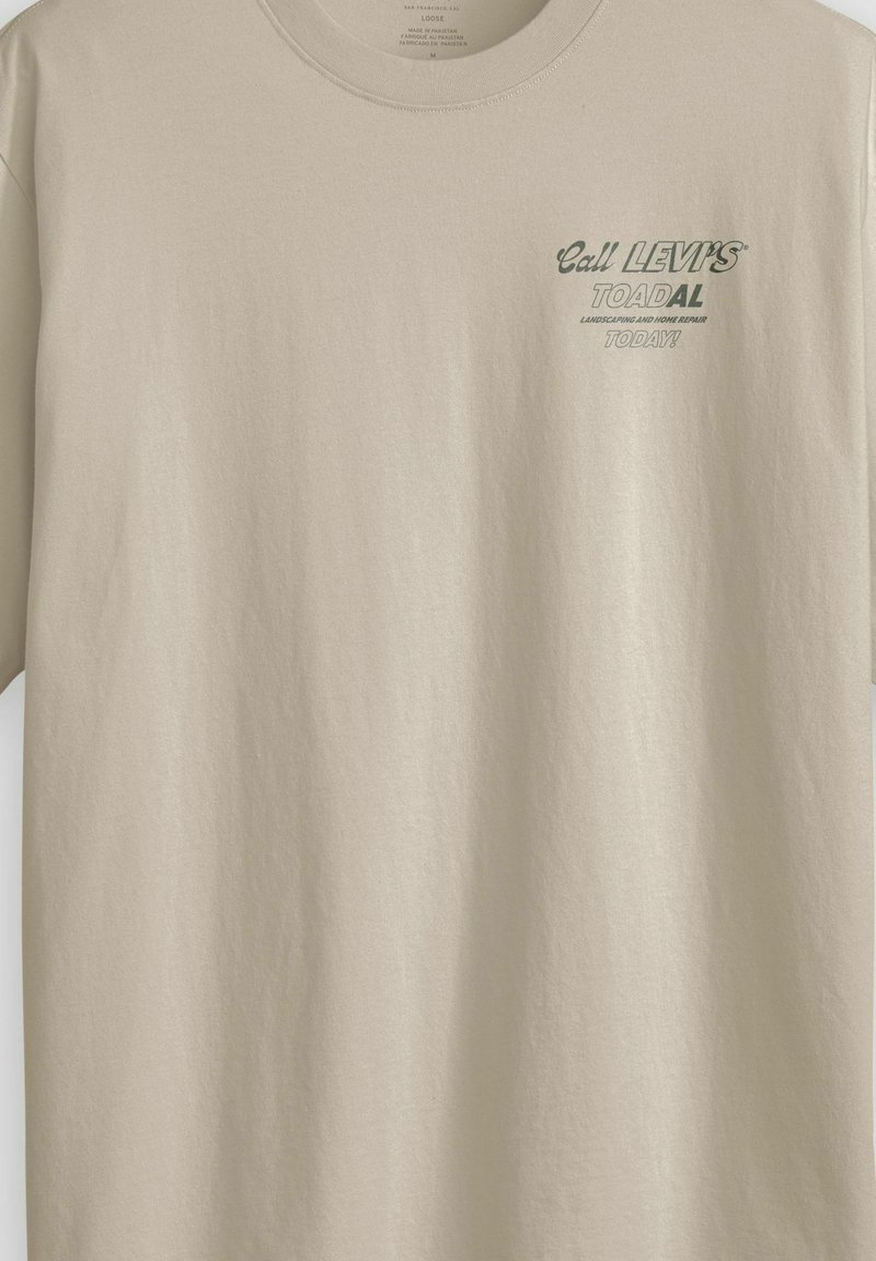 Maglietta beige a taglio largo con testo verde sul petto che recita "Chiama LEVI'S TOADAL paesaggistica e riparazioni domestiche OGGI!"