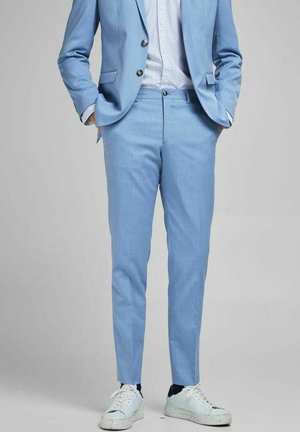 Light blue suit with matching trousers and white patterned shirt, paired with white sneakers featuring a speckled sole. Tailored fit, smooth texture.
