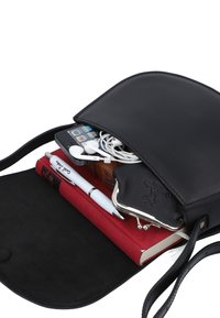 Borsa a tracolla in pelle nera con patta, contenente uno smartphone, auricolari, un taccuino rosso, una penna e un piccolo portamonete.