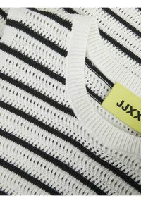 Top de punto blanco con rayas horizontales negras, un patrón de tejido abierto y un escote redondo. La etiqueta es amarilla con el logo "JJXX".