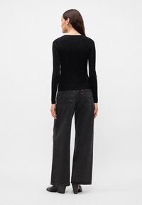 Črn dolg rokav ribast vrh v kombinaciji z visokim pasom širokimi črnimi kavbojkami. Opazne obročne uhane in elegantni črni gležnjarji dopolnjujejo obleko.