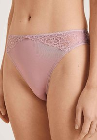 Lingerie rose avec des bordures en dentelle, dotée d'un corps en filet transparent et de bords crantés détaillés, présentant une taille élastique délicate et une texture lisse.