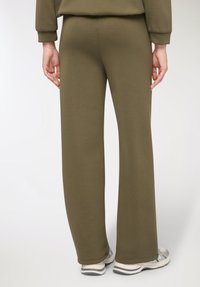 Pantaloni della tuta verde oliva in tessuto morbido, con vestibilità comoda, gambe svasate e texture liscia. Caratterizzati da un design semplice.
