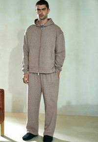 Brązowa bluza z kapturem na zamek błyskawiczny i dopasowane dresy wykonane z miękkiego materiału; charakteryzuje się luźnym krojem, kieszeniami kangurkami oraz kapturem ze sznurkiem.