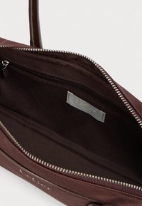 Καφέ τσάντα ώμου με ανοιχτό φερμουάρ που αποκαλύπτει εσωτερική τσέπη με φερμουάρ και ετικέτα μάρκας LeGer στη υφασμάτινη επένδυση.