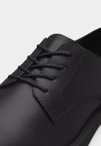 Μαύρο δερμάτινο παπούτσι με κλειστή κορδόνια και στρογγυλεμένη μύτη, που δείχνει λεία υφή και λεπτομερή ραφή στο επάνω μέρος.