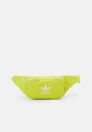 Banane Adidas jaune-vert vif avec poche zippée à l'avant et logo blanc sur un fond clair uni.