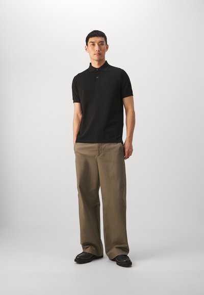Sort kortærmet polo med tre knapper, parret med lysebrune bredbukser og sorte sko. Enkel, afslappet stil.