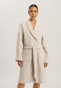 Robe beige di lunghezza media realizzato in tessuto testurizzato. Presenta un colletto a scialle, tasche anteriori e una cintura da annodare. Finitura liscia e morbida.