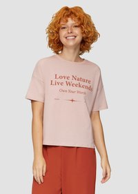 Roze katoenen t-shirt met korte mouwen, voorzien van een gedurfde bruine grafische tekstontwerp. Losse pasvorm met een ronde hals, gecombineerd met roestkleurige broek.