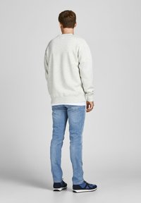 Light gray sweatshirt with long sleeves, ribbed cuffs, and hem; worn over a white shirt. Paired with light blue jeans and blue sneakers.