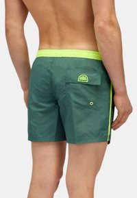 Pantaloni da nuoto verdi con una finitura testurizzata, caratterizzati da una vita elastica gialla brillante e un motivo laterale, e una tasca posteriore con dettagli logo.