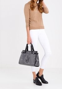 Černá perforovaná kabelka s dvojitými uchy, s hladkými akcenty a strukturovaným tvarem, doplněná o bílé džíny a černé boty.