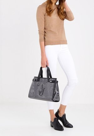 Czarna perforowana torebka z podwójnymi uchwytami, z gładkimi akcentami i usztywnionym kształtem, zestawiona z białymi jeansami i czarnymi butami.