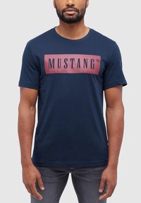 Navy blue cotton t-shirt featuring a maroon rectangular accent with the text "MUSTANG" in black, short sleeves, and a round neckline.